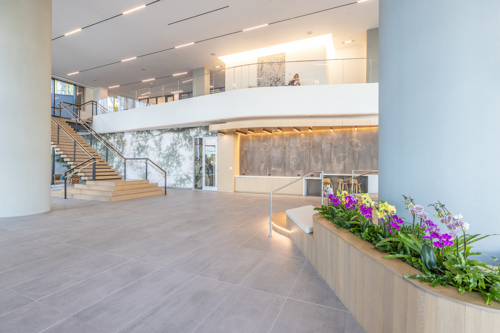 Double-height lobby at 800 Gessner Road with an open staircase and planters of orchids