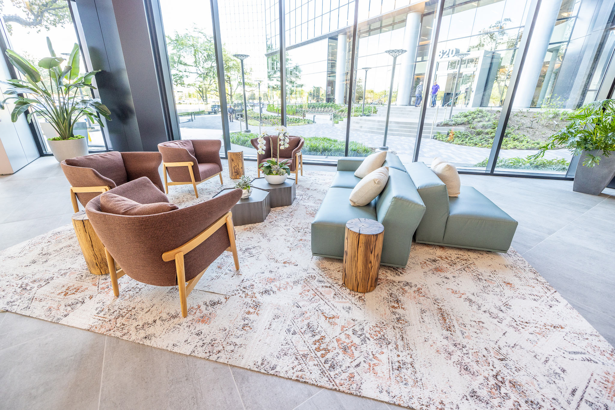 Lobby seating group at 800 Gessner Road with rust armchairs and a sage sofa beside planted greenery