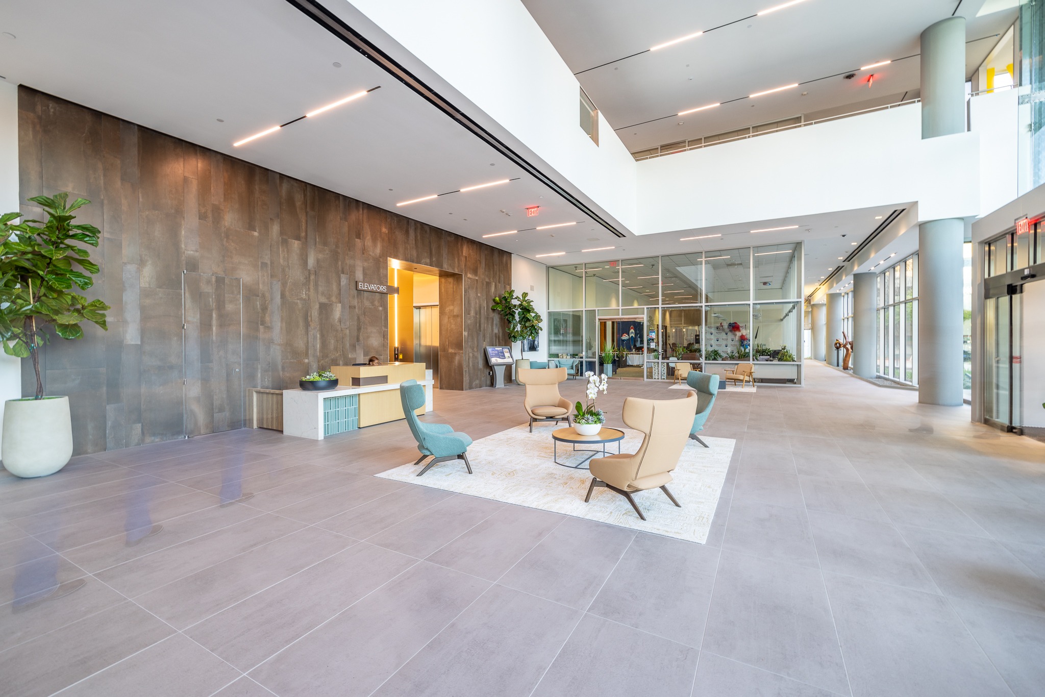 Lobby lounge at 820 Gessner Road with teal chairs, a concrete feature wall and reception beyond