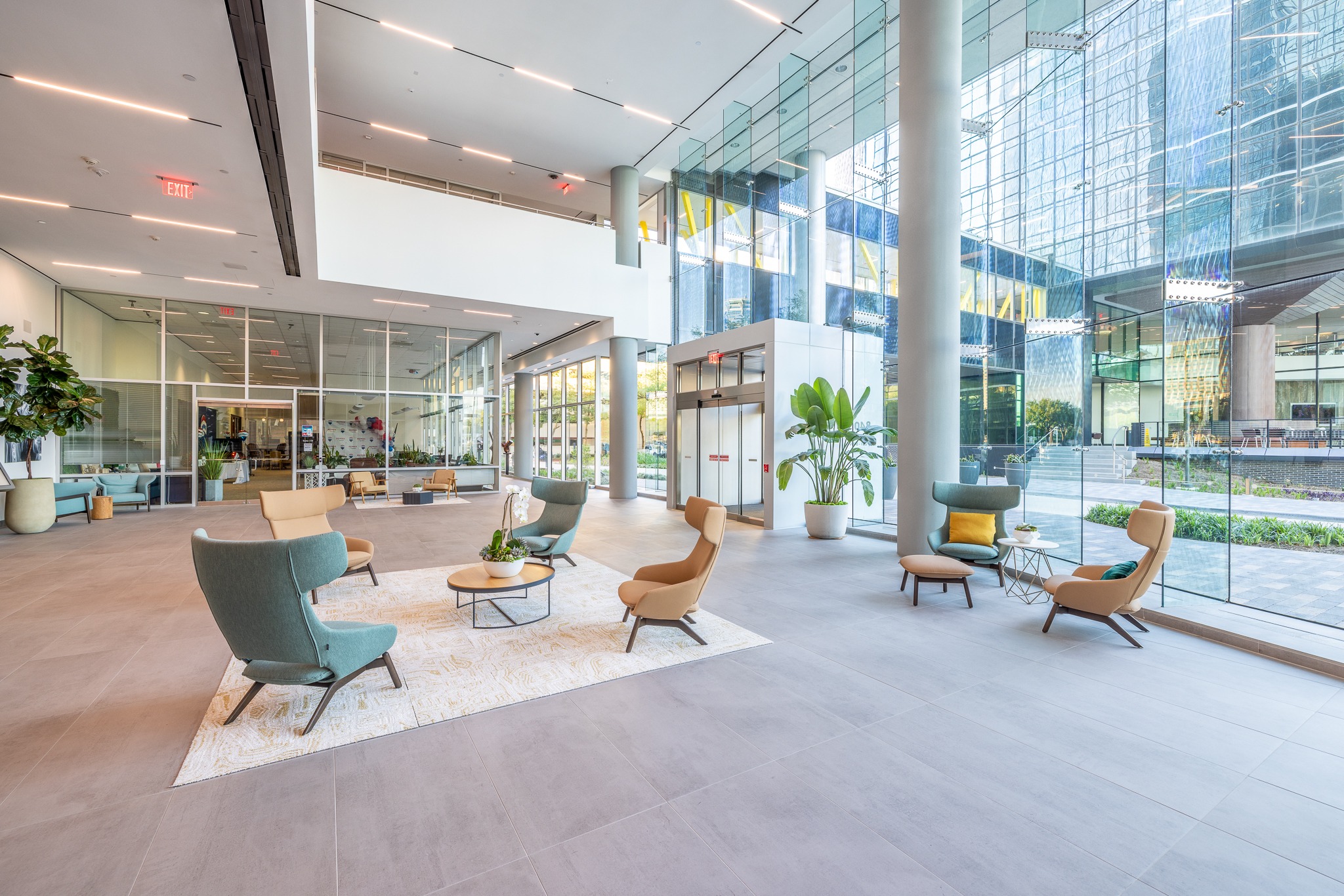 Lobby lounge at 840 Gessner Road with teal armchairs, an area rug and glass walls