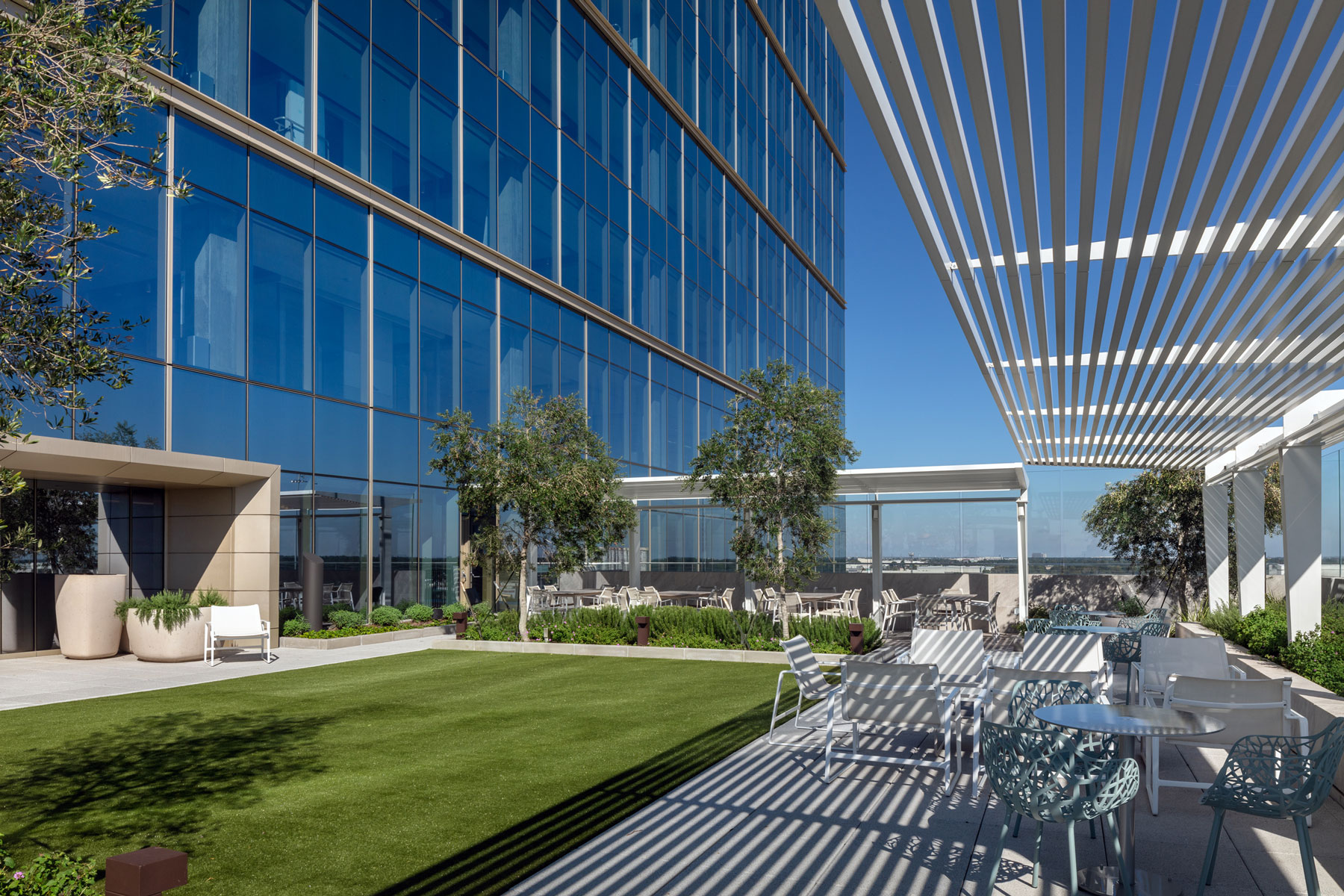 Outdoor amenity deck at 990 Town & Country with a lawn, louvered canopy and seating beside the glass tower