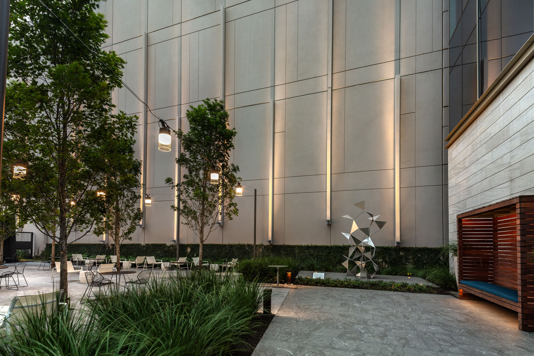 Courtyard at 990 Town & Country with tall trees, uplit stone walls and a sculpture
