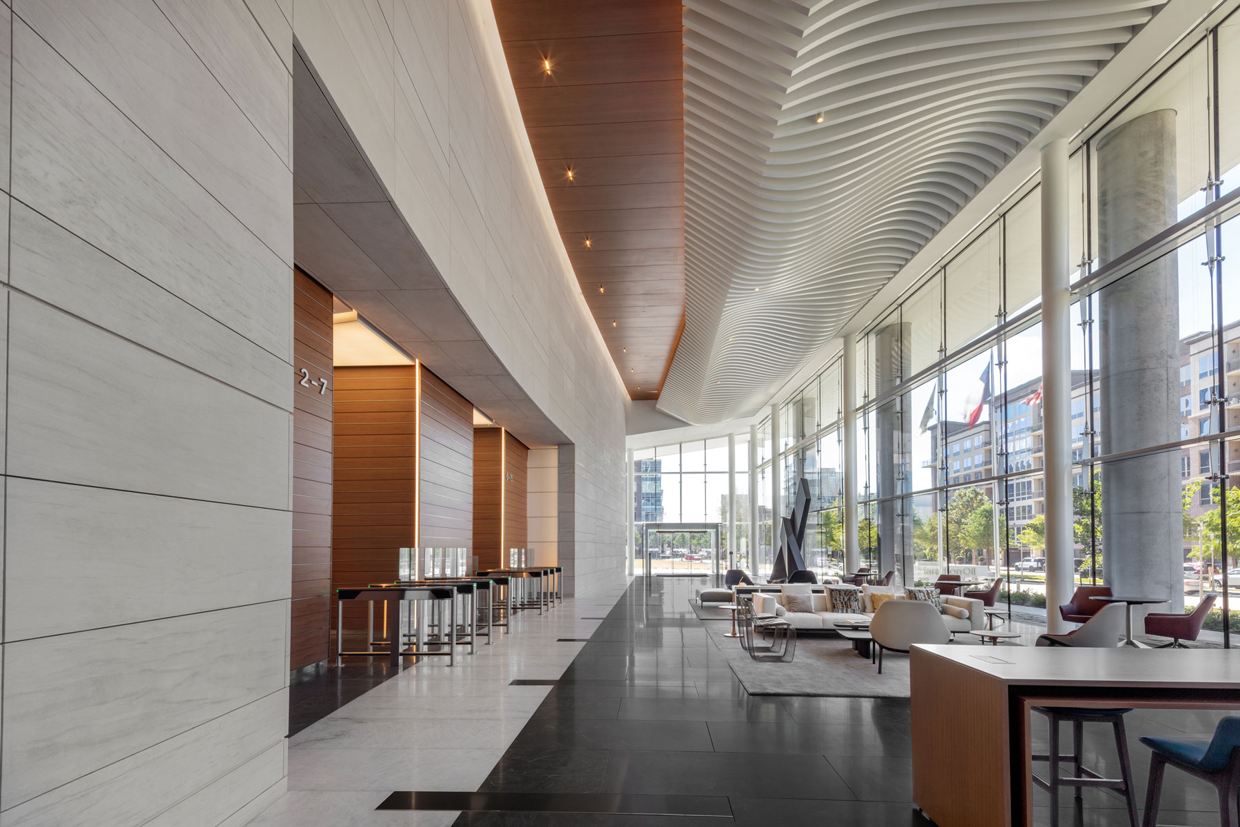 Lounge corridor at 990 Town & Country with a curved wood ceiling, stone wall and cafe seating along a window wall