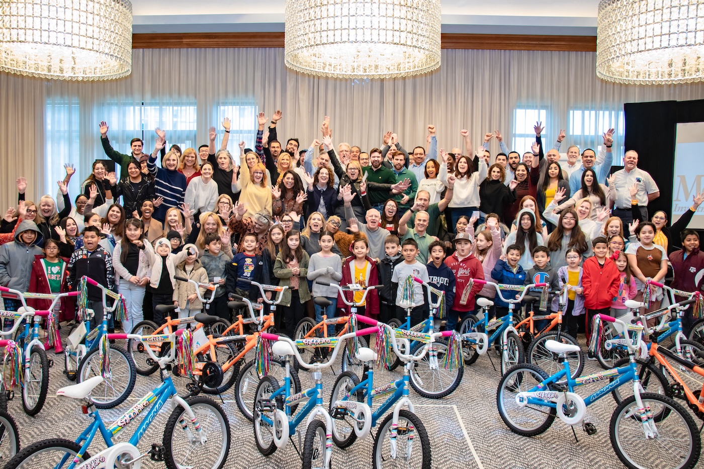 A large group of volunteers celebrating behind rows of assembled bicycles at a MetroNational community event