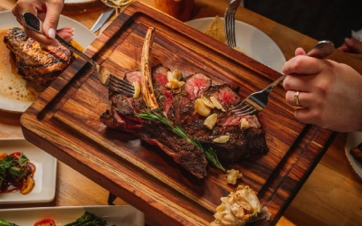Hands slicing into a grilled steak on a wooden serving board at Haywire in Gateway Memorial