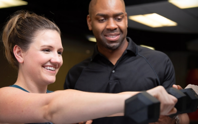 A trainer assisting a woman lifting a dumbbell in a fitness center