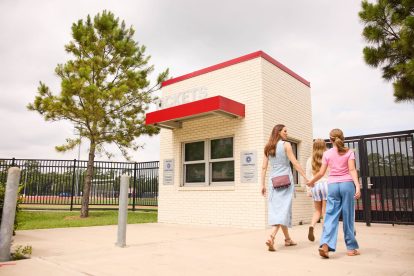 Two women walking past a small white building with a red entrance canopy