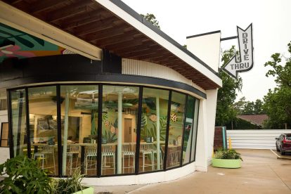 Exterior of a curved-glass restaurant with a hanging sign above the entrance