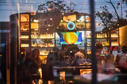 View through a window into a warmly lit bar where guests are seated