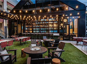 Haywire String-lit outdoor patio at Haywire beside Memorial City Mall, with tables set on a lawn in the evening