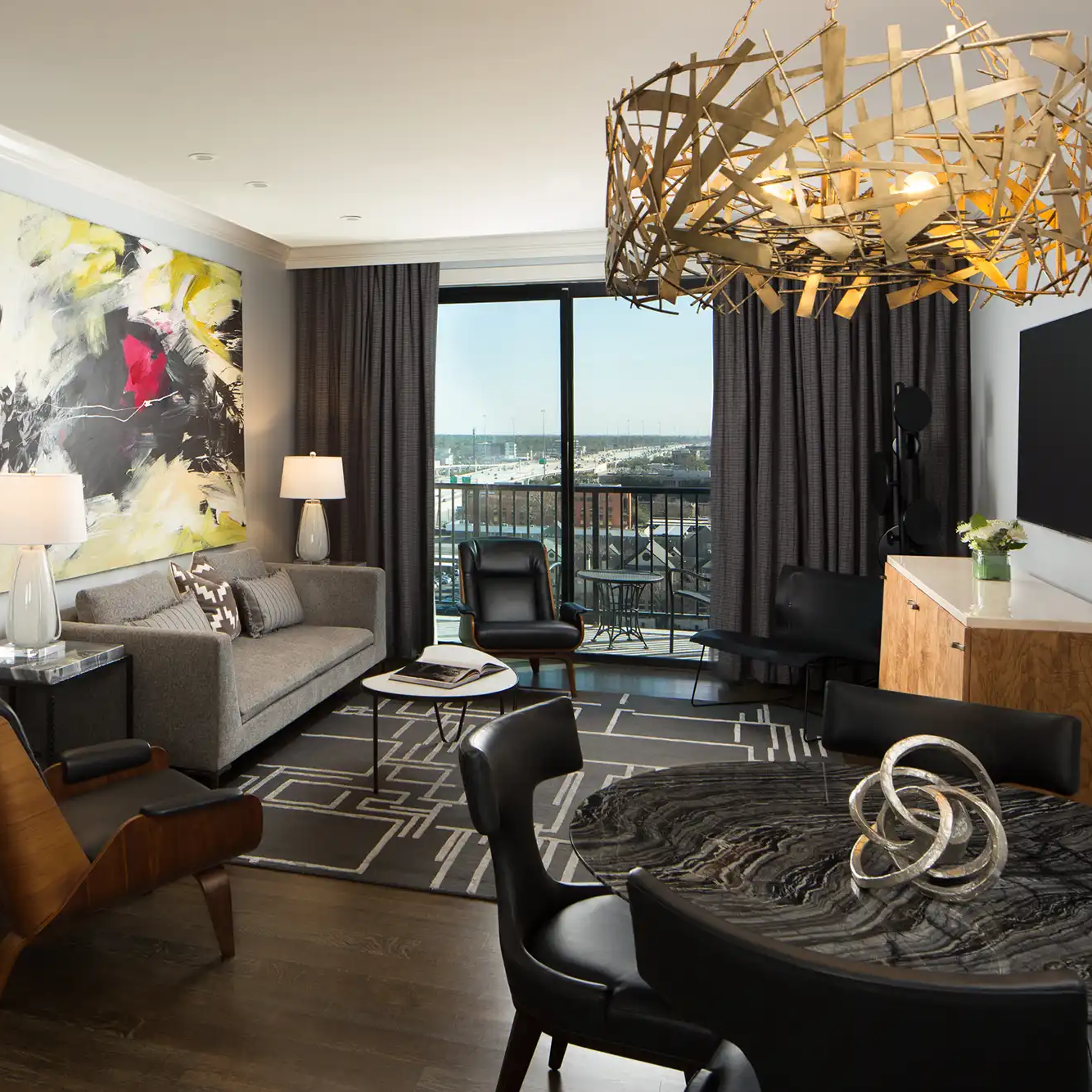 Suite living area at Hotel ZaZa Memorial with a sofa, dining table, chandelier and mural wall