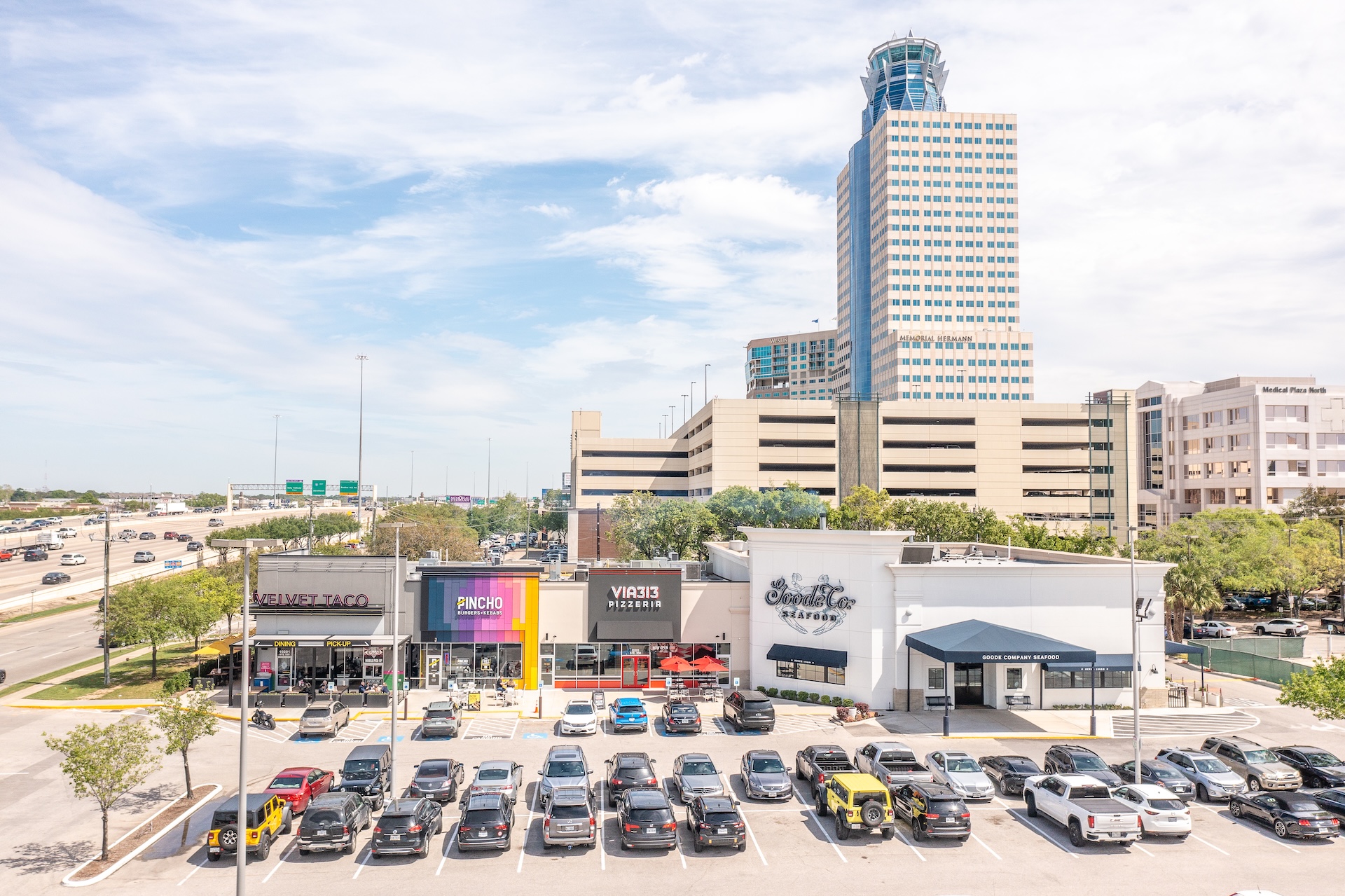 Elevated view of Katy Retail Centers with its parking lot in the foreground and a high-rise office tower behind