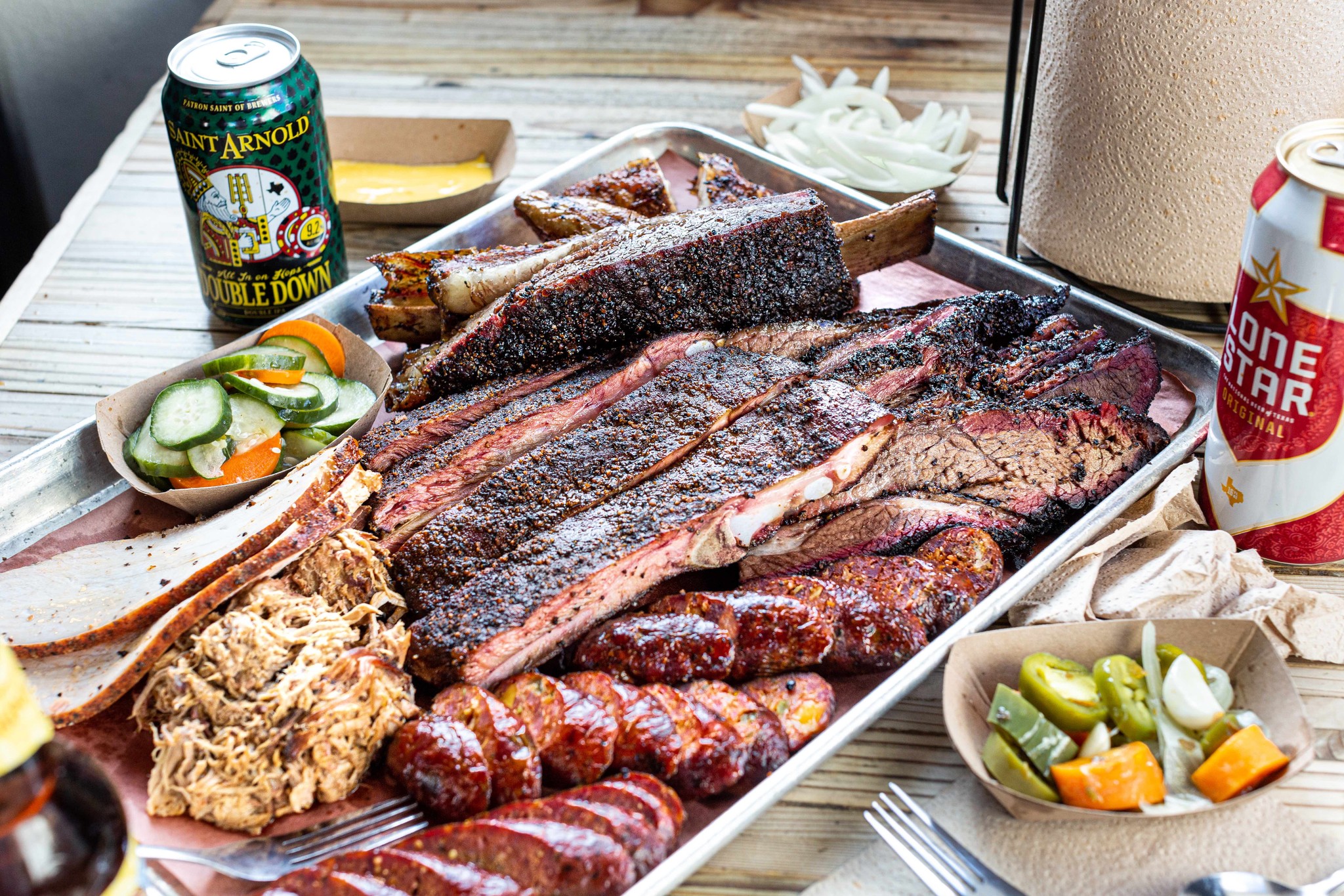 Barbecue platter of sliced brisket, sausage links and ribs with pickles and canned drinks