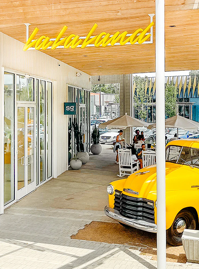 Vintage yellow truck parked inside La La Land at M-K-T Heights, beneath a neon sign