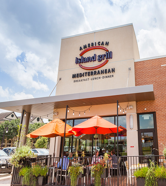 Exterior of American Island Grill Mediterranean at Memorial City Village, with orange patio umbrellas