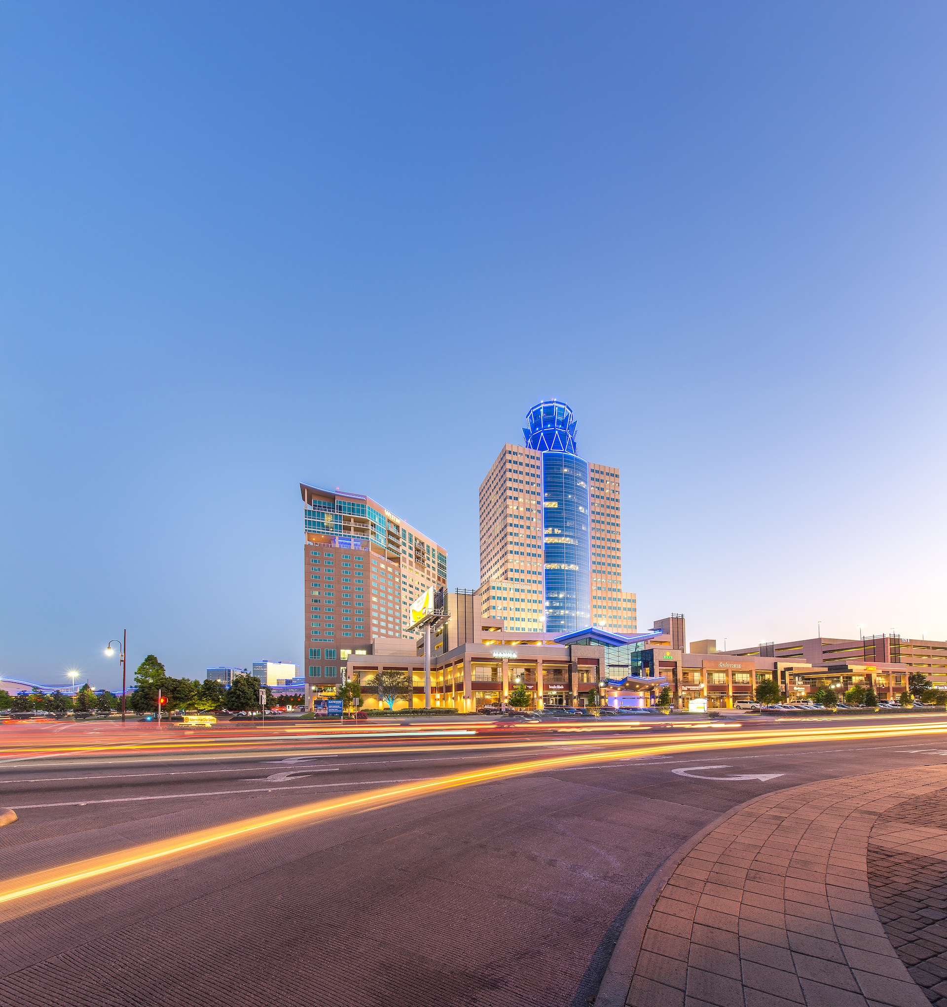 View along a road at dusk toward the blue-lit Memorial Hermann Tower
