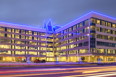Office building illuminated at night with coloured accent lighting and traffic light trails