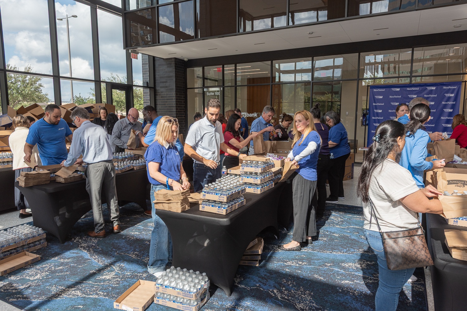 Volunteers packing supplies at long tables in a MetroNational lobby