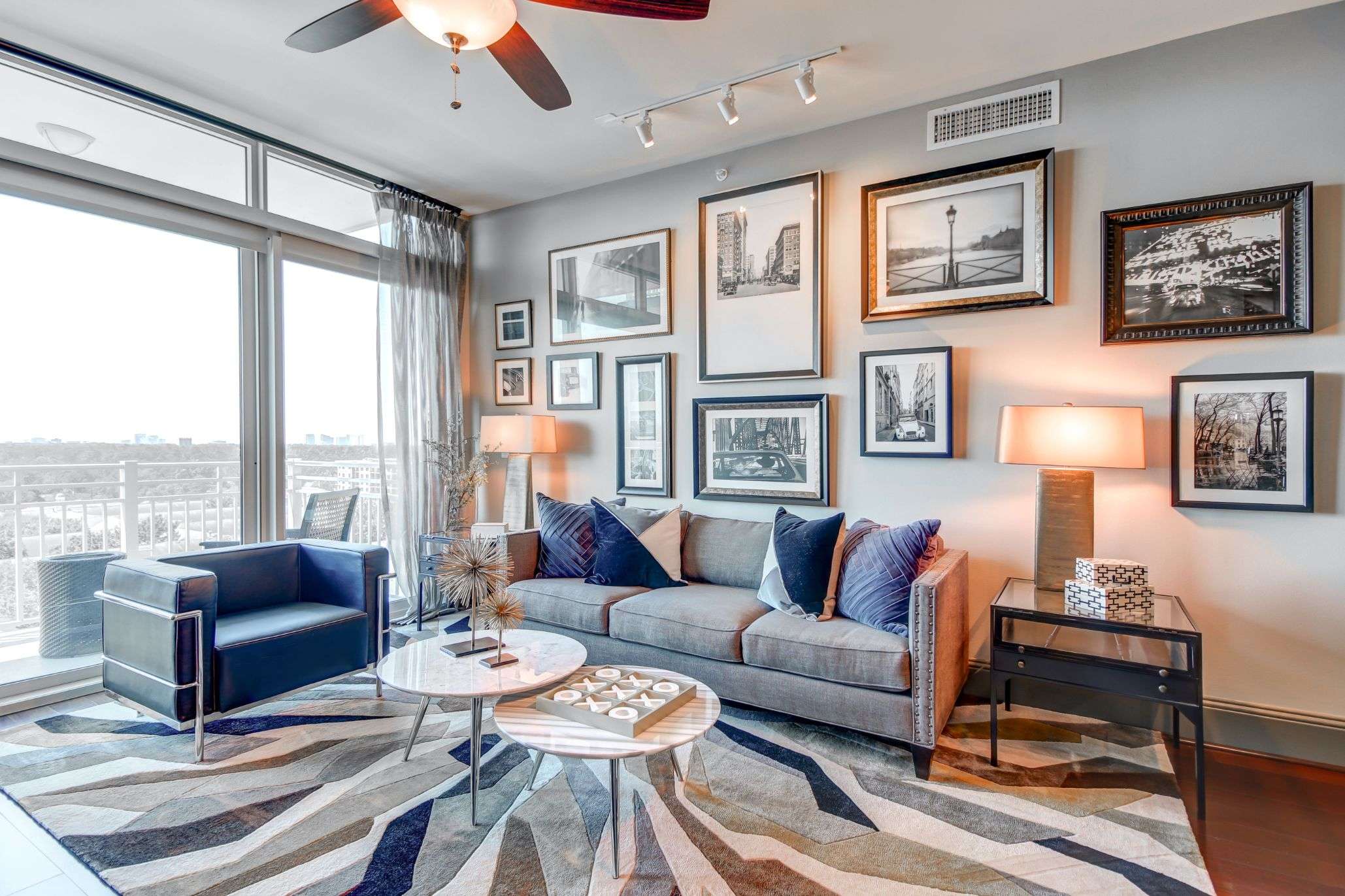 Living room at The Fountains with a sofa, gallery wall of framed photographs and corner windows