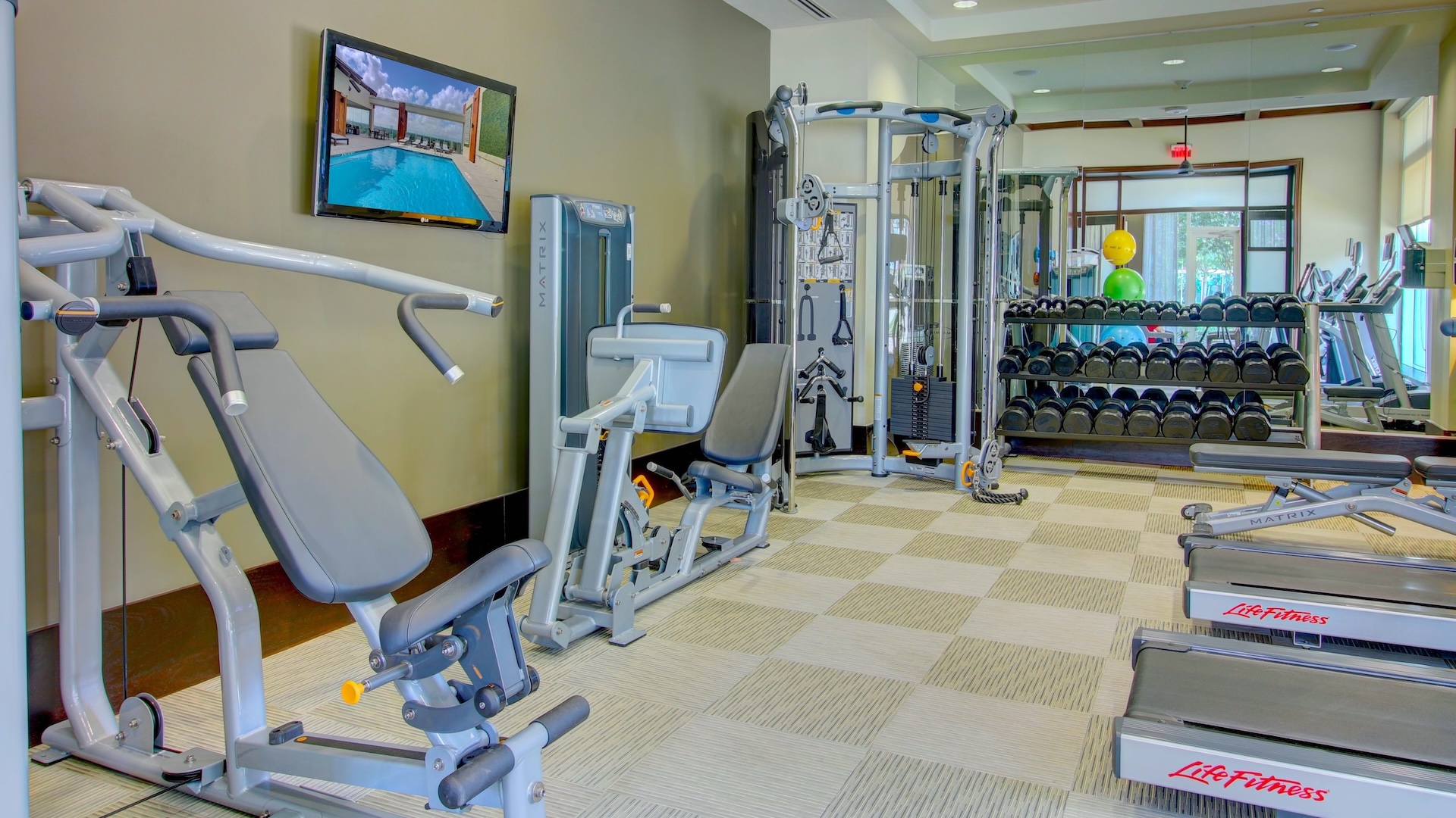 Fitness room at The Fountains with weight machines, free weights and a wall-mounted television