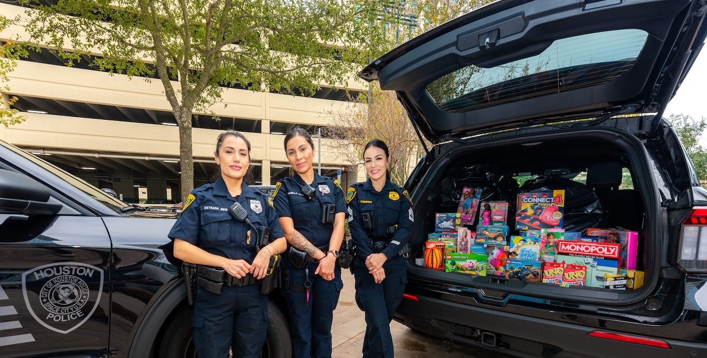 Three police officers standing behind an SUV loaded with donated toys at a MetroNational toy drive