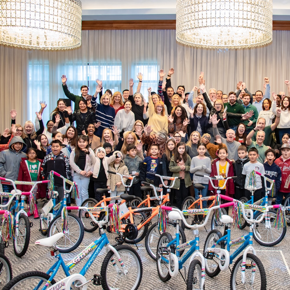 WhyMN-ConnectCommunity A large group of volunteers raising their arms behind rows of donated bicycles at a MetroNational community event