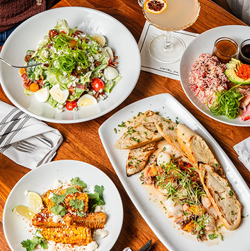 ZaZaMemorialCity-Fall2025-FoodPic-MAIN-1 1 Overhead spread of salads and entrees on white plates at Hotel ZaZa Memorial