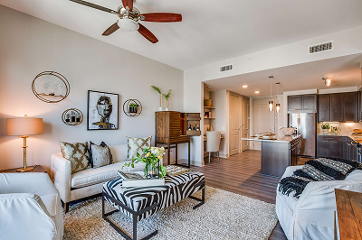 Apartment living room with a sofa and ceiling fan, opening onto the kitchen beyond